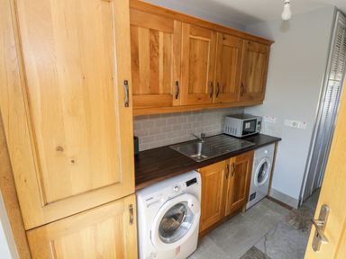A utility room with wooden cabinets a washing machine a microwave and a sink at The Visiting House in Gorteen near Dunmore County Galway