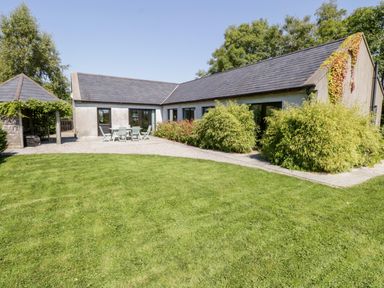 A single-story house with a slate roof a grassy lawn bushes and a patio with outdoor furniture at The Visiting House in Gorteen near Dunmore County Galway