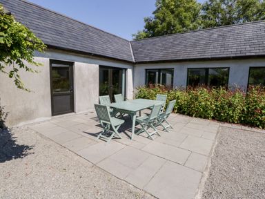 An outdoor patio with a table and six chairs beside a building with windows and doors at The Visiting House in Gorteen near Dunmore County Galway