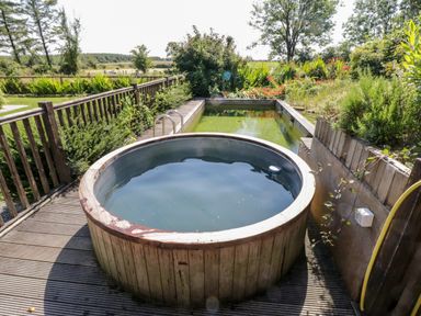 An outdoor wooden hot tub on a deck next to a small rectangular pool with greenery around at The Visiting House in Gorteen near Dunmore County Galway