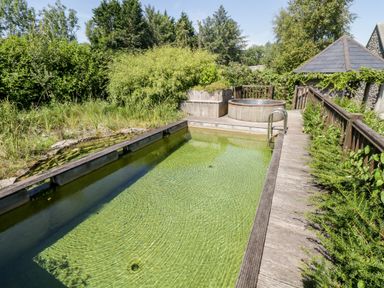 An outdoor swimming pool with wooden decking beside a hot tub and garden vegetation at The Visiting House in Gorteen near Dunmore County Galway