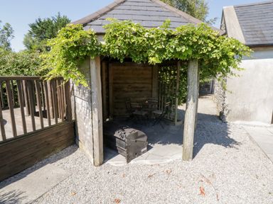 A small wooden gazebo with green vines on the roof and a table with four chairs inside at The Visiting House in Gorteen near Dunmore County Galway