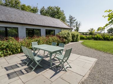 An outdoor patio with a green table and six chairs next to a building and garden at The Visiting House in Gorteen near Dunmore County Galway