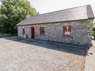 A stone cottage with red framed windows and door on a gravel driveway at The Visiting House in Gorteen near Dunmore County Galway