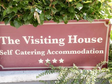 A sign reading The Visiting House Self Catering Accommodation partially covered by green leaves at The Visiting House in Gorteen near Dunmore County Galway