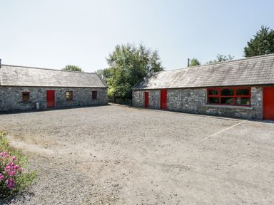 An outdoor courtyard with two stone buildings with red doors and windows at The Visiting House in Gorteen near Dunmore County Galway