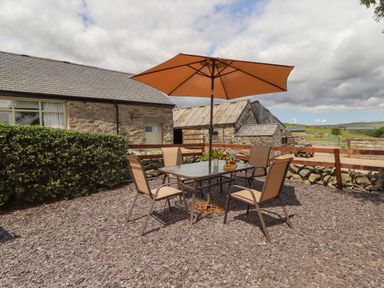 An outdoor patio area with a table and four chairs under an orange umbrella next to stone buildings at Y Bwthyn in Ysbyty Ifan