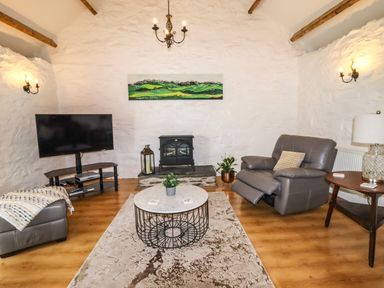 A living room with a grey recliner chair a round coffee table a television on a stand a wooden side table and a fireplace at Y Bwthyn in Ysbyty Ifan