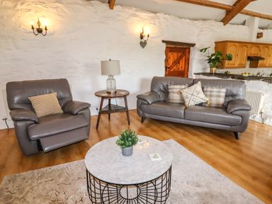 A living room with two gray leather sofas a round marble coffee table with a plant a wooden side table with a lamp and a wooden kitchen cabinet in the background at Y Bwthyn in Ysbyty Ifan