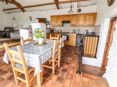 A kitchen with wooden cabinets a dining table with chairs and a flower vase at Y Bwthyn in Ysbyty Ifan