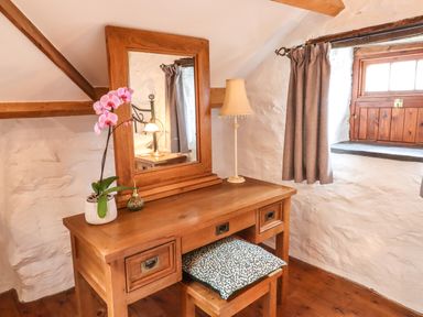 A wooden dressing table with a mirror and lamp next to a window with curtains at Y Bwthyn in Ysbyty Ifan