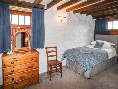 A bedroom with a single bed a wooden chair a wooden dresser with a mirror and blue curtains at Y Bwthyn in Ysbyty Ifan
