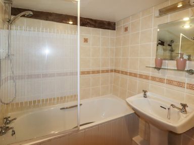A bathroom with a bathtub and shower combination a sink with two taps a mirror and a glass shelf with two pink containers at Y Bwthyn in Ysbyty Ifan