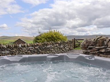 A bubbling hot tub outdoors with a stone wall and countryside view at Y Bwthyn in Ysbyty Ifan