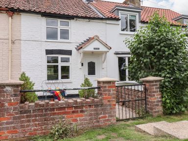 A white brick cottage with a tiled roof a small garden with two chairs a table a brick wall and a metal gate at The Cottage Kilham near Driffield