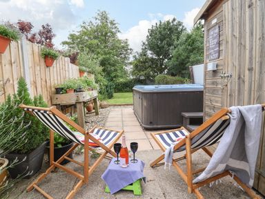 A garden patio with two wooden deck chairs and a small table with glasses and a bottle near a hot tub at The Cottage in Kilham near Driffield