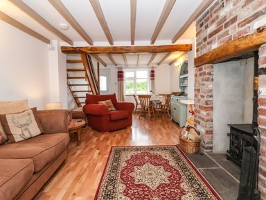 A living room with wooden beams a red and beige rug and a brick fireplace at The Cottage Kilham near Driffield