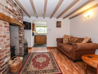 A living room with a brown sofa and round wooden table next to a brick fireplace and a rug on the floor at The Cottage in Kilham near Driffield