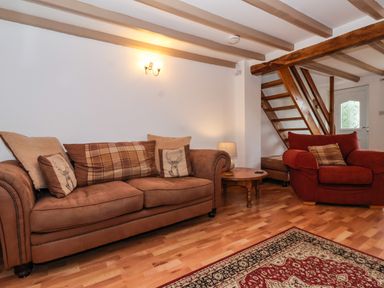 A living room with two sofas a wooden coffee table a lamp wooden stairs and a patterned rug at The Cottage in Kilham near Driffield