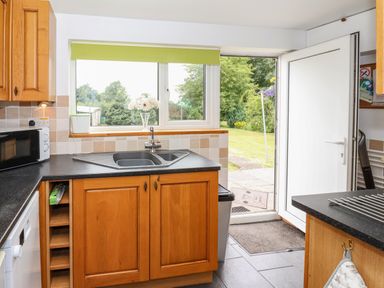A kitchen with wooden cabinets a double sink a microwave and a door open to a garden at The Cottage Kilham near Driffield