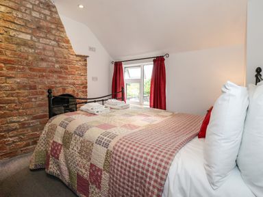A bedroom with a bed covered in a patchwork quilt red curtains and an exposed brick wall at The Cottage Kilham near Driffield