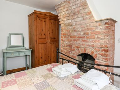 A bedroom with a patchwork quilt on the bed folded towels on the bed a wooden wardrobe a green dressing table and an exposed brick fireplace at The Cottage Kilham near Driffield