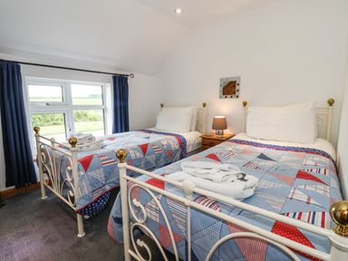 A bedroom with two single metal beds and a window with blue curtains at The Cottage in Kilham near Driffield