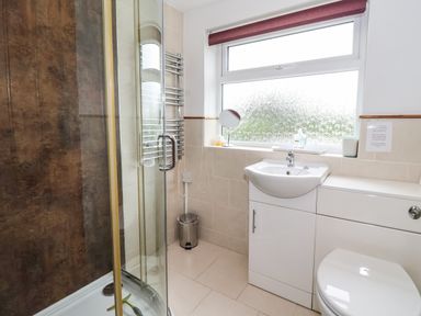 A bathroom with a shower enclosure a white sink and a toilet under a frosted window at The Cottage in Kilham near Driffield