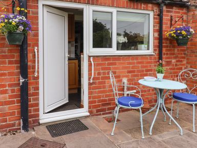 A small patio with a round table and two metal chairs with blue cushions outside a brick wall with a white door and window at The Cottage Kilham near Driffield