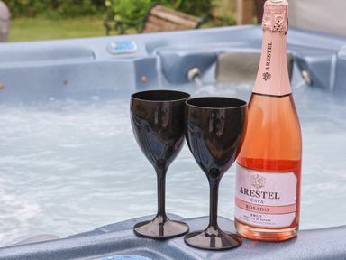 A bottle of rosado cava and two black wine glasses on the edge of a hot tub at The Cottage in Kilham near Driffield