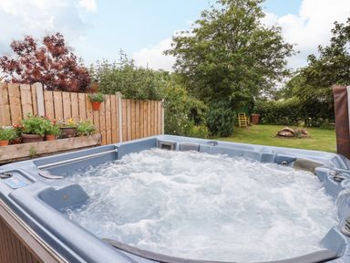 An outdoor hot tub next to a wooden fence with potted plants and a garden with trees and grass at The Cottage in Kilham near Driffield