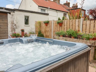 An outdoor hot tub with bubbling water next to a wooden fence with flower pots and plants at The Cottage in Kilham near Driffield