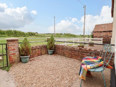 An outdoor seating area with a metal chair and a colorful blanket next to a low brick wall with two potted plants at The Cottage Kilham near Driffield