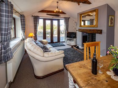 A living room with cream sofa wooden dining table and glass doors leading to a patio at Cwm Derw Cottage in Llanafan Fawr near Builth Wells
