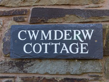 A black rectangular sign with white letters mounted on a stone wall reading Cwm Derw Cottage at Llanafan Fawr near Builth Wells