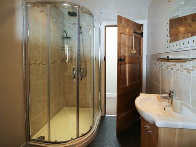 A bathroom with a curved glass shower enclosure a wooden door and a sink with a mirror at Cwm Derw Cottage in Llanafan Fawr near Builth Wells