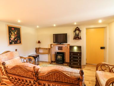 A living room with wicker furniture a wall clock a television above a fireplace and a yellow door at Sutton Cottage in Ballysheen near Rosslare Harbour County Wexford
