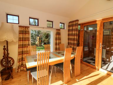 A dining room with a glass table and wooden chairs next to windows and wooden doors at Sutton Cottage Ballysheen near Rosslare Harbour County Wexford