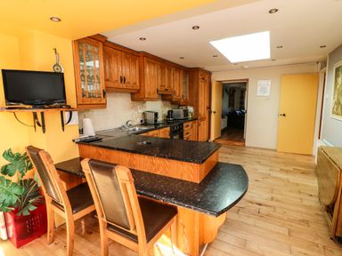 A kitchen with wooden cabinets black countertops a small TV and two chairs at Sutton Cottage Ballysheen near Rosslare Harbour County Wexford