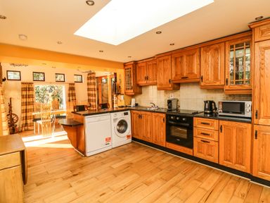 A kitchen with wooden cabinets black countertop dishwasher washing machine oven and dining area at Sutton Cottage Ballysheen near Rosslare Harbour County Wexford