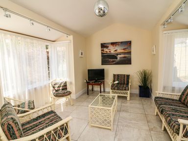 A sunroom with rattan chairs and sofa a glass coffee table a small TV on a wooden stand and a plant at Sutton Cottage Ballysheen near Rosslare Harbour County Wexford