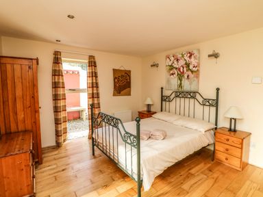 A bedroom with a metal frame bed two bedside tables with lamps wooden wardrobe and door with curtains at Sutton Cottage Ballysheen near Rosslare Harbour County Wexford