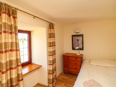 A bedroom with a window with curtains a wooden chest of drawers a bed and a framed picture on the wall at Sutton Cottage in Ballysheen near Rosslare Harbour County Wexford