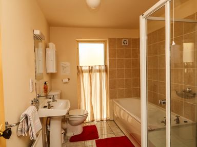 A bathroom with a sink, toilet, bathtub, shower enclosure, and window with curtains at Sutton Cottage Ballysheen near Rosslare Harbour County Wexford