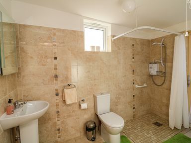 A bathroom with a sink, toilet, window, shower area with curtain, and tiled walls at Sutton Cottage in Ballysheen near Rosslare Harbour, County Wexford