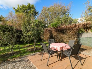 An outdoor patio area with a round table covered by a checkered cloth and four chairs surrounded by trees and bushes at Sutton Cottage Ballysheen near Rosslare Harbour County Wexford