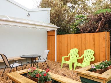 An outdoor patio area with gravel ground two green plastic chairs a round table with two chairs and wooden planters with flowers at Sutton Cottage in Ballysheen near Rosslare Harbour County Wexford
