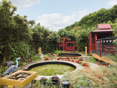 A garden with two circular ponds red garden gate red swing statues and dense greenery at Sutton Cottage in Ballysheen near Rosslare Harbour County Wexford