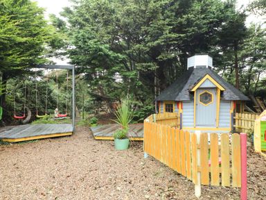 A garden with a small playhouse and swings surrounded by trees at Sutton Cottage in Ballysheen near Rosslare Harbour County Wexford