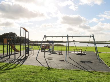 An outdoor playground with swings slides and climbing structures near a body of water at Sutton Cottage Ballysheen near Rosslare Harbour County Wexford